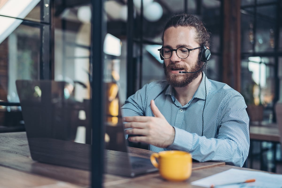 a person wearing a headset and glasses sitting at a table with a laptop